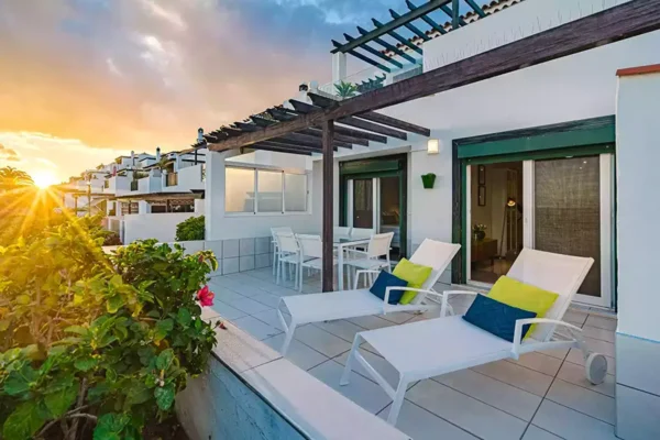 Terraza moderna de una casa o villa al atardecer con tumbonas, zona de comedor exterior y pérgola de madera.